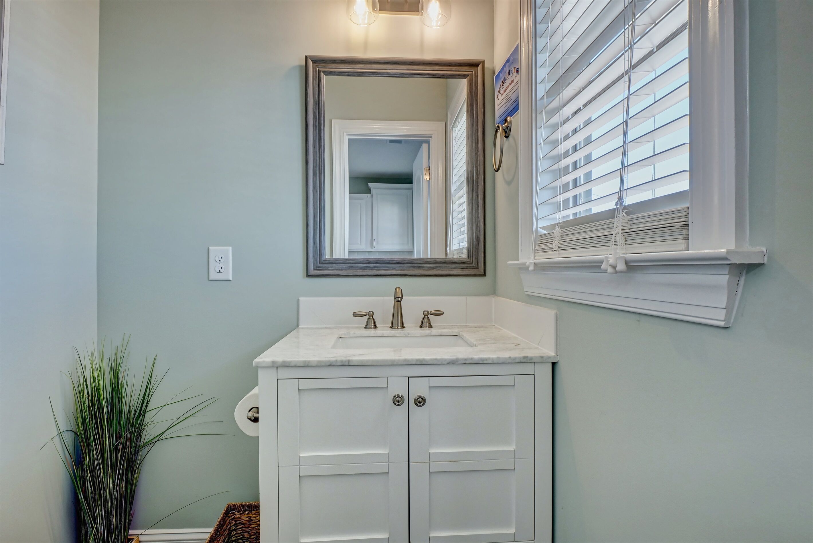A bathroom with a white vanity, a large mirror, and a window with blinds.