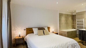 Un dormitorio con una cama grande, una mesita de noche, una lámpara en la mesilla y un baño con bañera y perchero para toallas.
