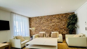 Un salón moderno con pared de piedra, un sofá blanco, una mesa de centro y suelo de madera.