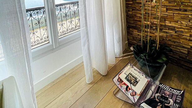 Una habitación con pared de madera, una ventana con cortinas blancas, una orquídea en maceta y una revista sobre una mesa.