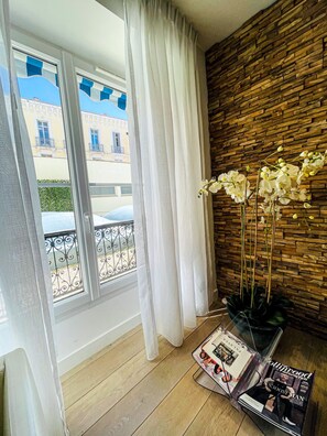 A room with a wooden wall, a window with white curtains, a potted orchid, and a magazine on a table.