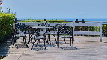 A wooden deck with outdoor furniture and a view of the ocean.