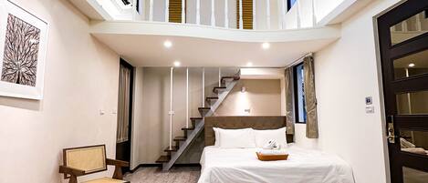 Una habitación de hotel moderna con diseño tipo loft, que incluye una cama, una zona de estar y una escalera que lleva a un nivel superior.