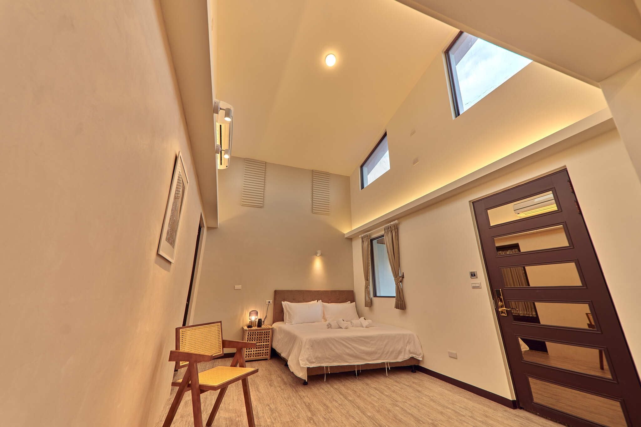 Un dormitorio con cama, una silla, una mesita de noche, una ventana y una puerta.