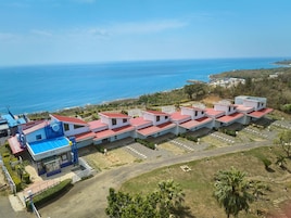 A coastal hotel with multiple red-roofed buildings, a blue-roofed structure, and a view of the sea.