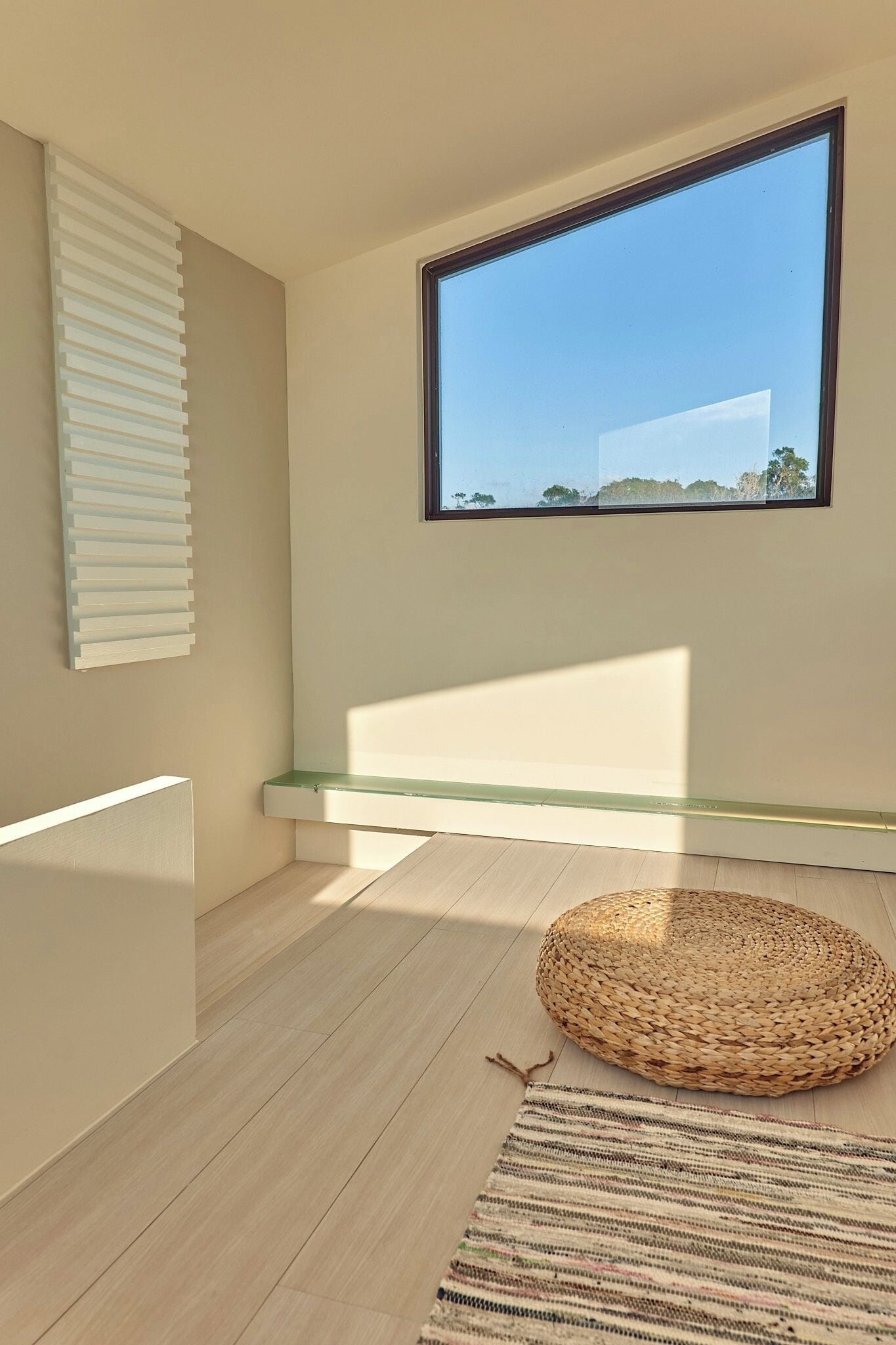 Una habitación moderna con un ventanal grande, una cesta tejida y una alfombra a rayas.