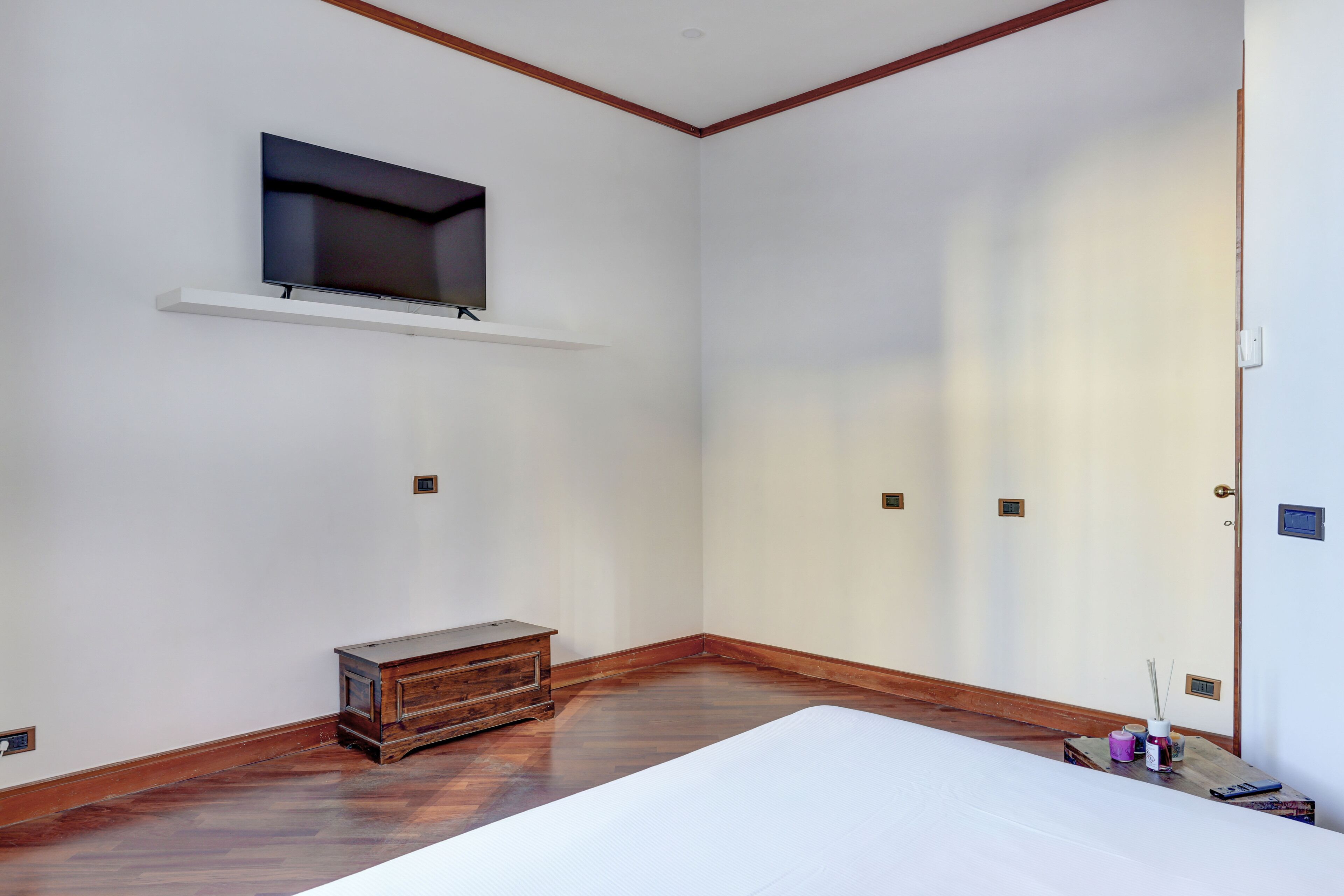 A room with a bed, a wooden dresser, a mounted TV, and a door with a small window.