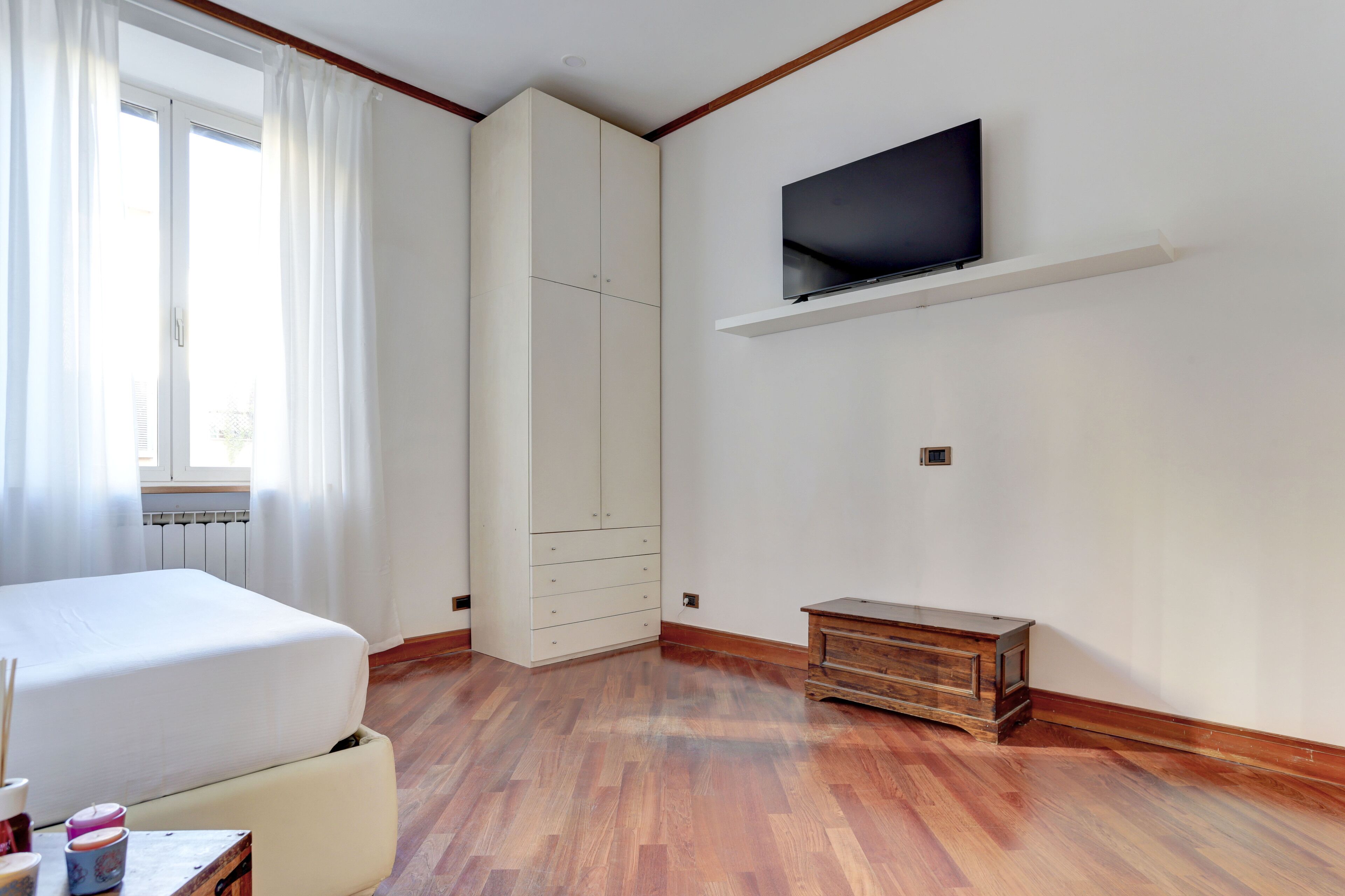 A bedroom with a bed, a wardrobe, a TV mounted on the wall, and a wooden cabinet.
