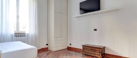 A bedroom with a bed, a wardrobe, a TV mounted on the wall, and a wooden cabinet.