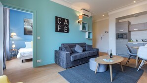 Ein modernes Wohnzimmer mit einem grauen Sofa, einem kleinen runden Tisch und einer blauen Wand mit dem Schriftzug 'CAFE'.