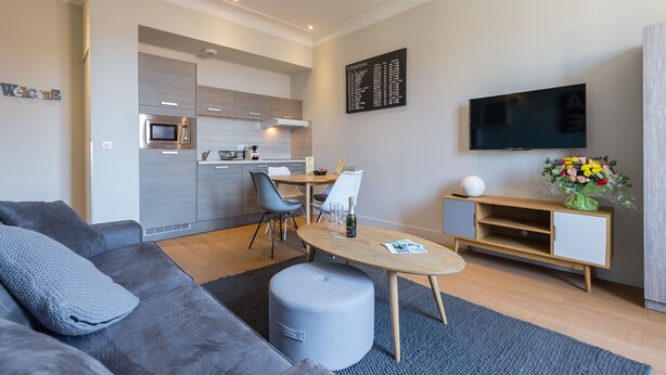 Ein modernes Wohnzimmer mit einem grauen Sofa, einem Holzesstisch und einer Küche im Hintergrund.