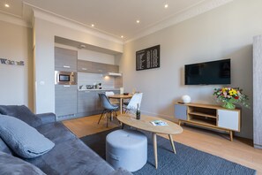 A modern living room with a grey sofa, a wooden dining table, and a kitchen in the background.