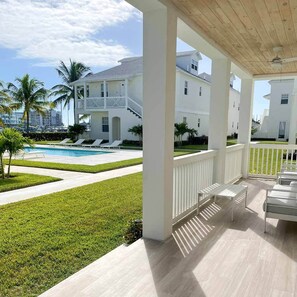 Un espace extérieur abrité doté d’une piscine, de colonnes blanches et offrant une vue sur une grande maison blanche avec un balcon.