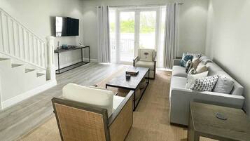 Een moderne woonkamer met een bank, salontafel en televisie. Een trap leidt naar een ander niveau.