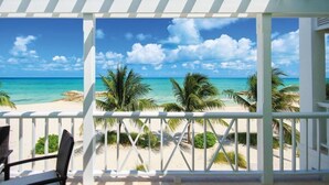 Une vue sur la plage depuis un espace abrité, agrémenté de rampes de protection blanches, de palmiers et d’un ciel bleu azur.