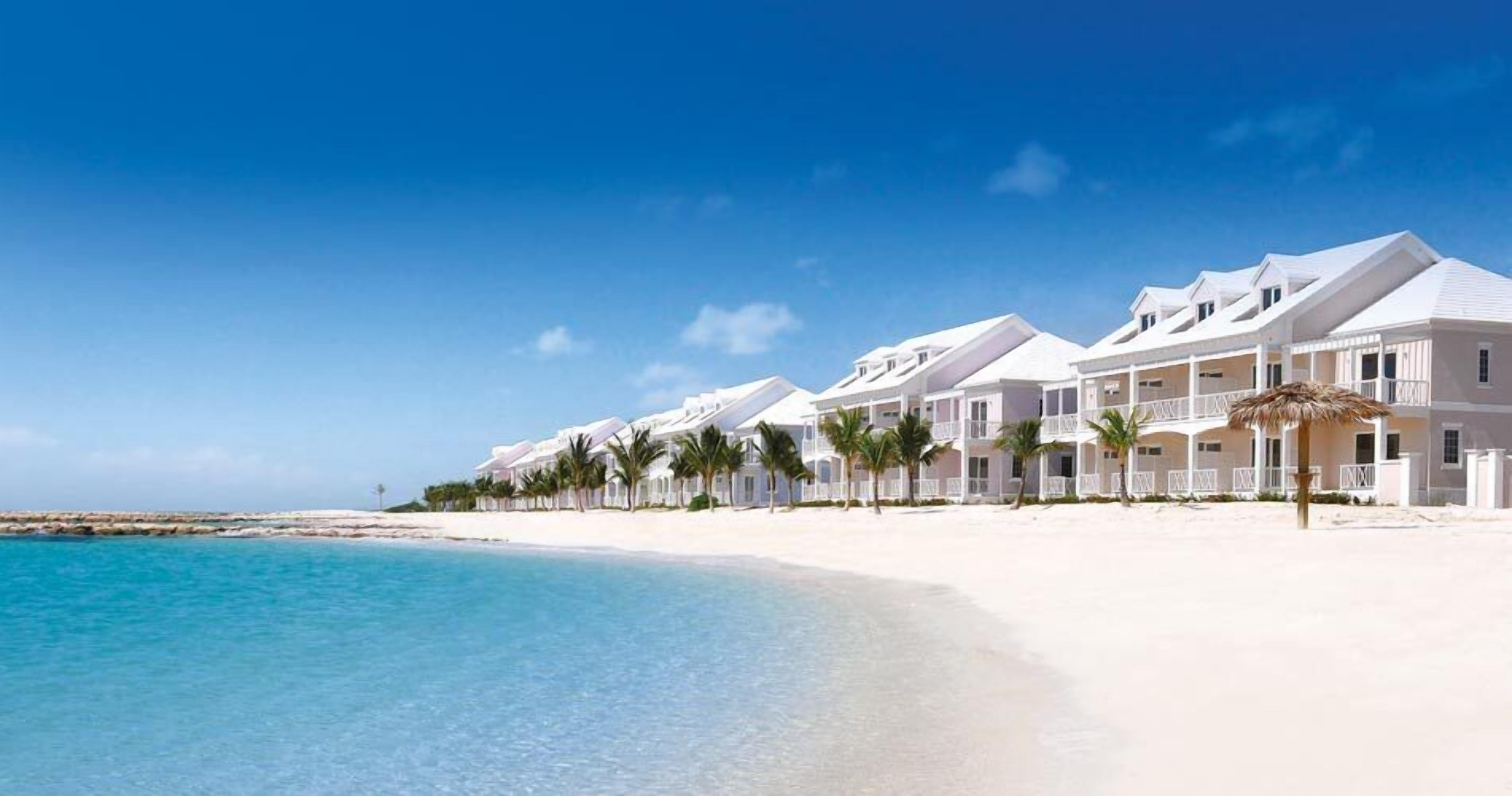 A beachfront hotel with white buildings, a sandy beach, and clear blue water.