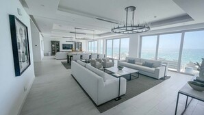 Un salon moderne avec un grand canapé, une table basse et un coin repas offrant une vue sur l’océan.
