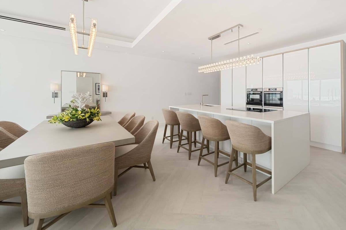 Een moderne keuken met een centraal eiland, een bar met krukken, en een eethoek met een lange tafel en stoelen.