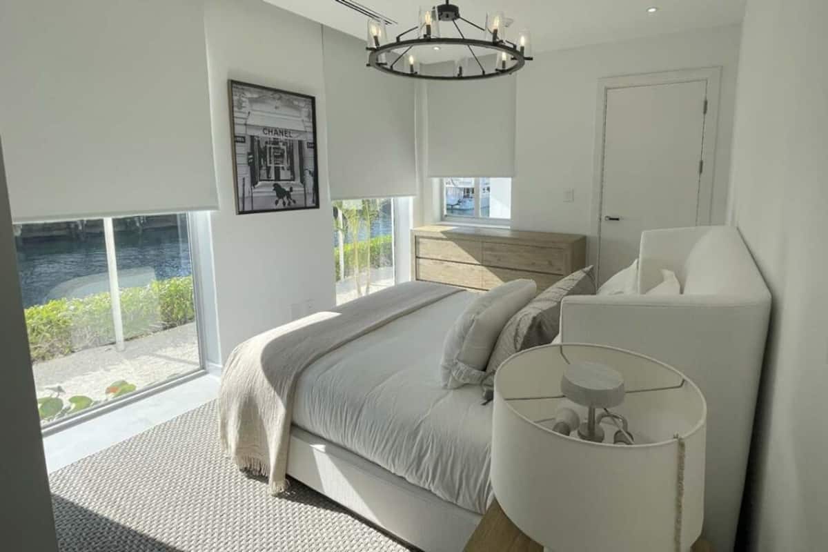 Een moderne slaapkamer met een groot bed, nachtkastje, raam met uitzicht op groen en een kroonluchter.
