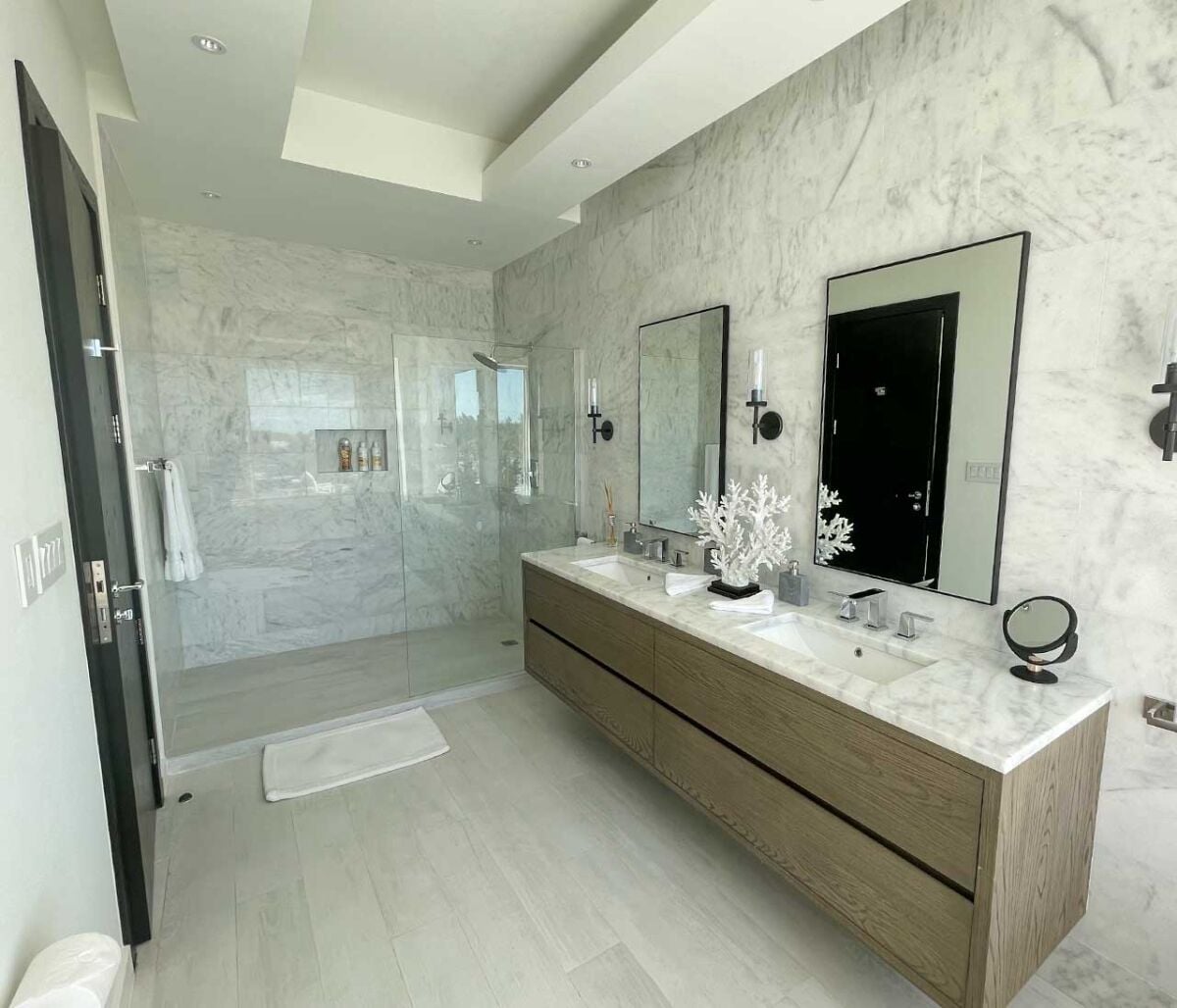 Un bagno moderno con doppio lavabo, ampi specchi e cabina doccia in vetro.