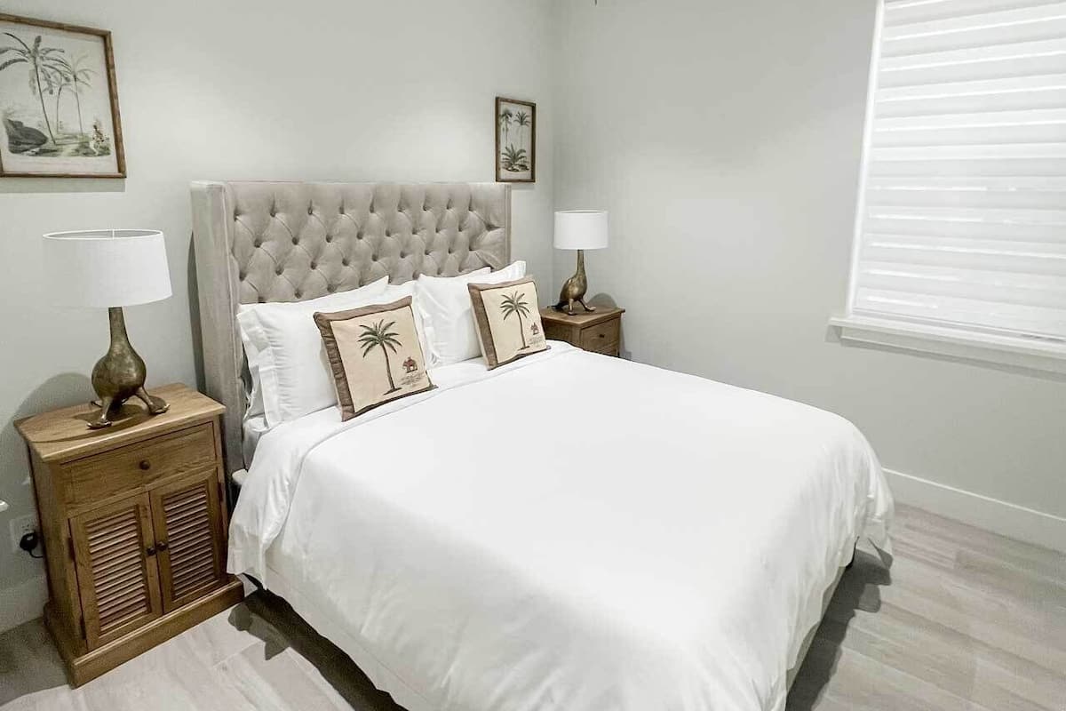 Een slaapkamer met een groot bed, twee nachtkastjes, een plafondventilator en een raam met zonwering.