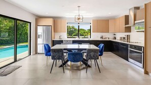 A modern kitchen with a dining area, large windows, and a view of a swimming pool.