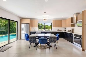 A modern kitchen with a dining area, large windows, and a view of a swimming pool. - Swish Villa | Unique BKB Court | Outdoor Cinema (Miami)