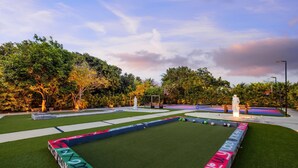 A well-maintained outdoor area with a green artificial turf, a basketball court, and a statue.