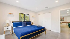 A modern bedroom with a large bed, bedside tables, a wardrobe, and a window with blinds.