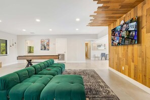 A modern living room with a green sofa, a pool table, and a wooden wall with a TV.