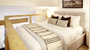Een slaapkamer met een houten hoofdbord, een bed met witte lakens en gestreepte kussens, een bedlampje en een ingelijste foto aan de muur.