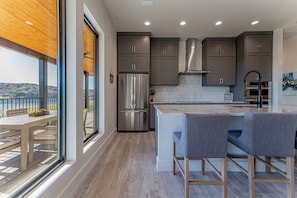 A modern kitchen with a large island, stainless steel appliances, and a view of the outdoors. - Gather, Relax & Play in a Modern Home with Hot Tub, Bunk Room & Outdoor Space (Lago Vista)