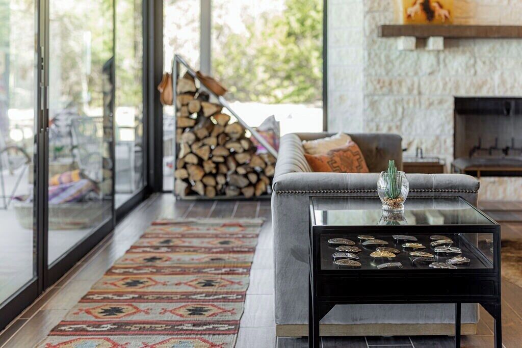 A modern living room with a glass coffee table, a grey sofa, and a patterned rug.