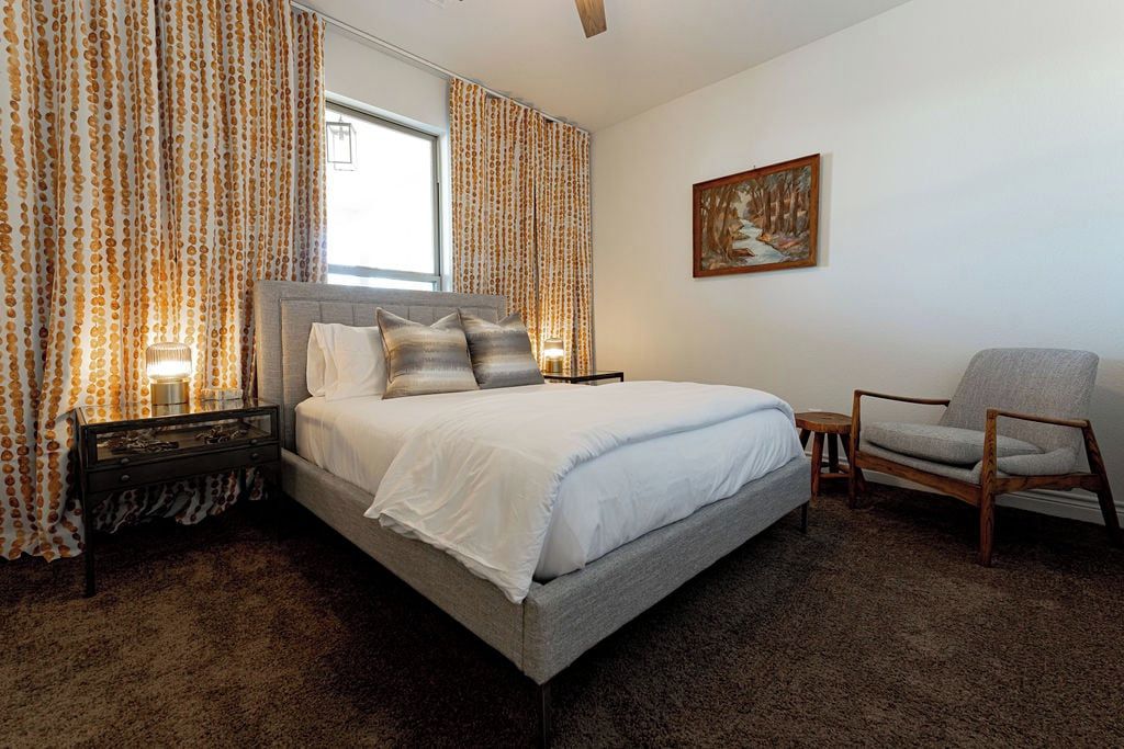 A bedroom with a bed, a chair, a painting on the wall, and curtains.