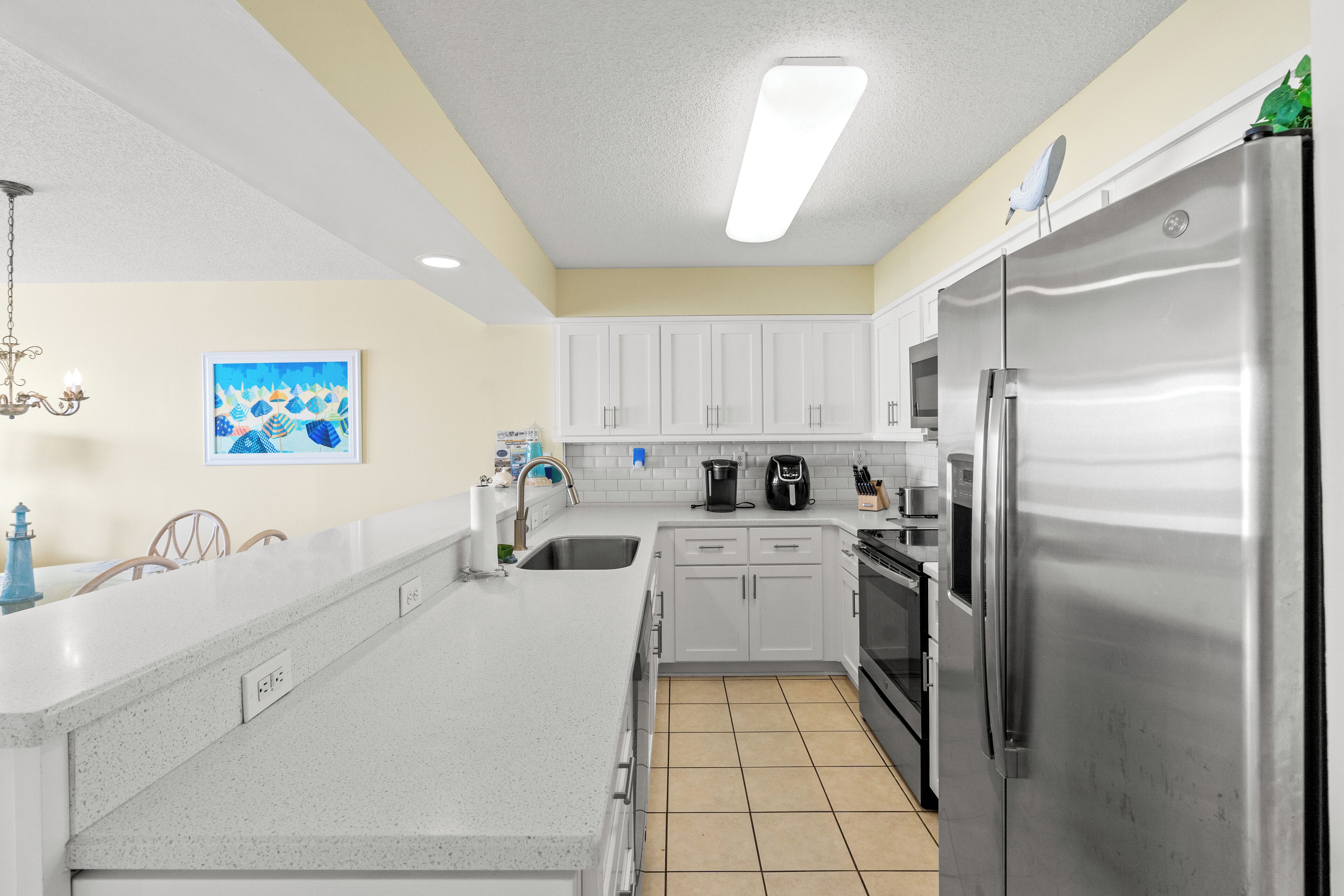 A modern kitchen with white cabinets, a stainless steel refrigerator, a coffee maker, and a sink.