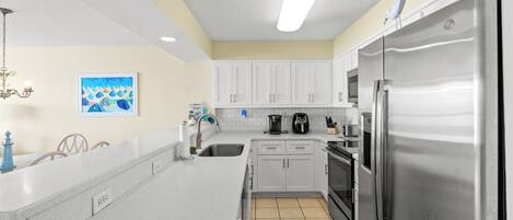 A modern kitchen with white cabinets, a stainless steel refrigerator, a coffee maker, and a sink.