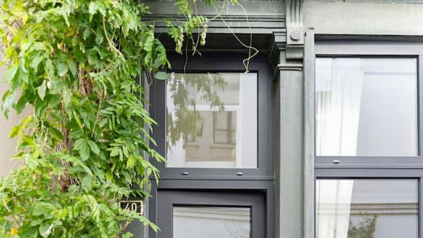 Una entrada de edificio moderno con una puerta oscura, un escalón pequeño y una caja metálica en el suelo.