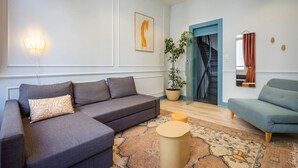 Una sala de estar moderna con un sofá gris, un sillón azul, una mesa de centro redonda y una planta en maceta.