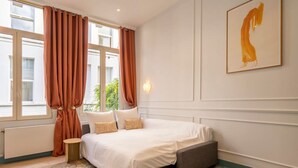 Un dormitorio con una cama grande, una mesita de noche, una pequeña mesa y una ventana con cortinas.