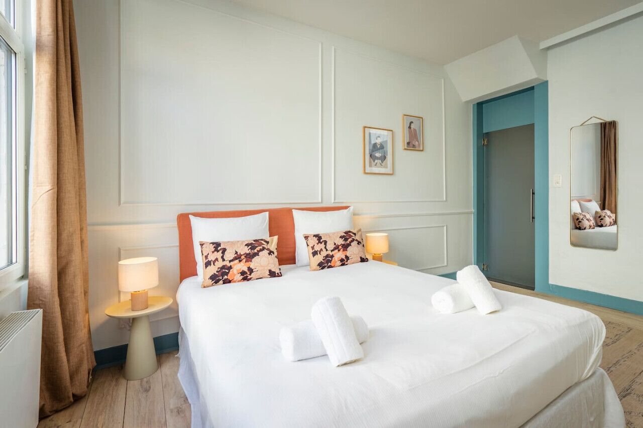 A hotel room with a large bed, two bedside tables with lamps, a door, and a mirror on the wall.