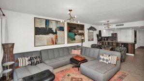 A modern living room with a grey sectional sofa, a coffee table, and a rug. There are abstract paintings on the wall and a kitchen area in the background. - Oceanfront, stunning, renovated, Guests love it! (Ponte Vedra Beach)