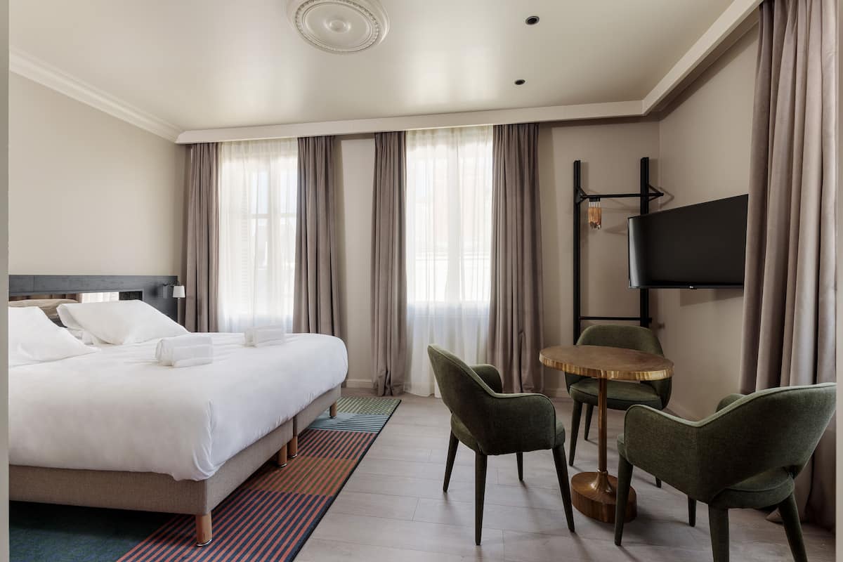 Ein Hotelzimmer mit einem Bett, zwei Stühlen, einem kleinen Tisch und einem Fernseher an der Wand.