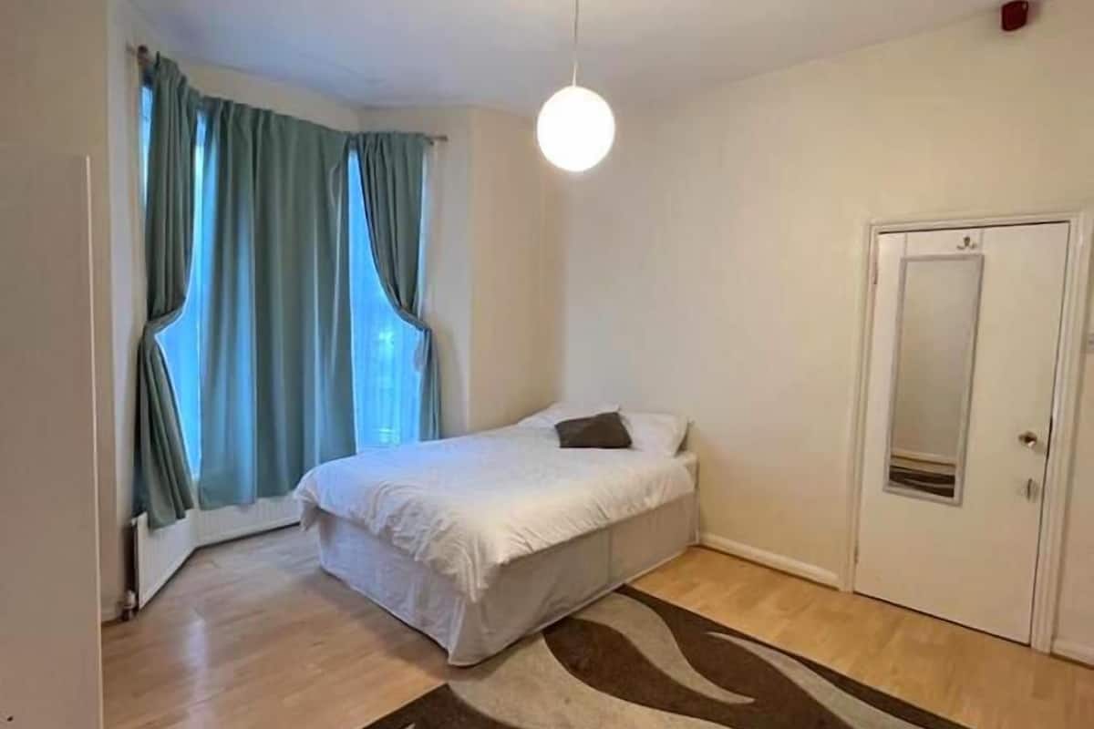 Un dormitorio con cama, lámpara colgante, puerta y ventana con cortinas.