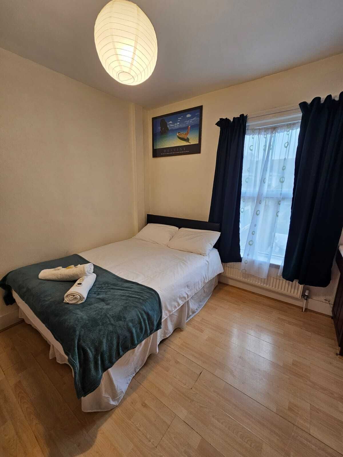 Une chambre à coucher avec un lit, un radiateur, une fenêtre avec des rideaux et un tableau accroché au mur.