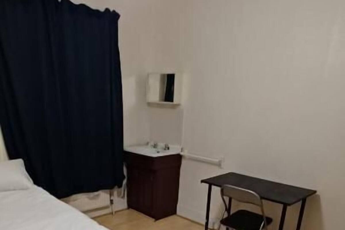 Un dormitorio con cama, escritorio, silla, cómoda y lámpara colgante.