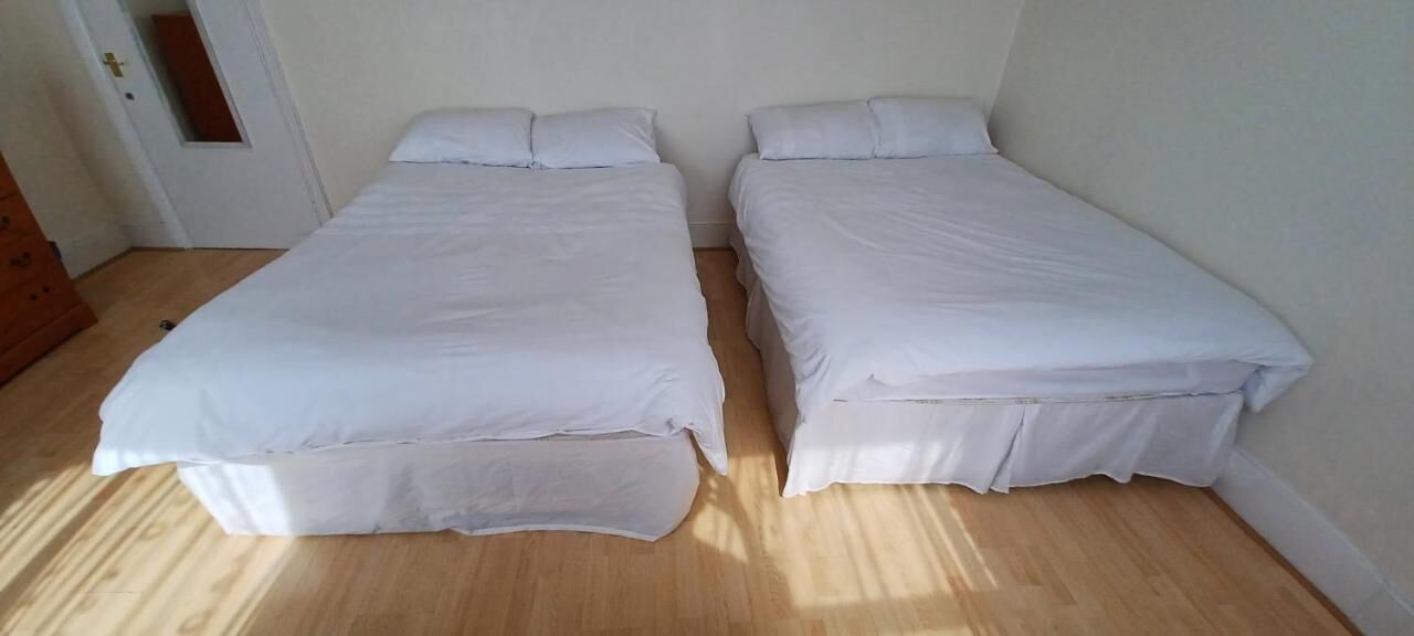 Een kamer met twee éénpersoonsbedden, houten vloer en een witte deur.