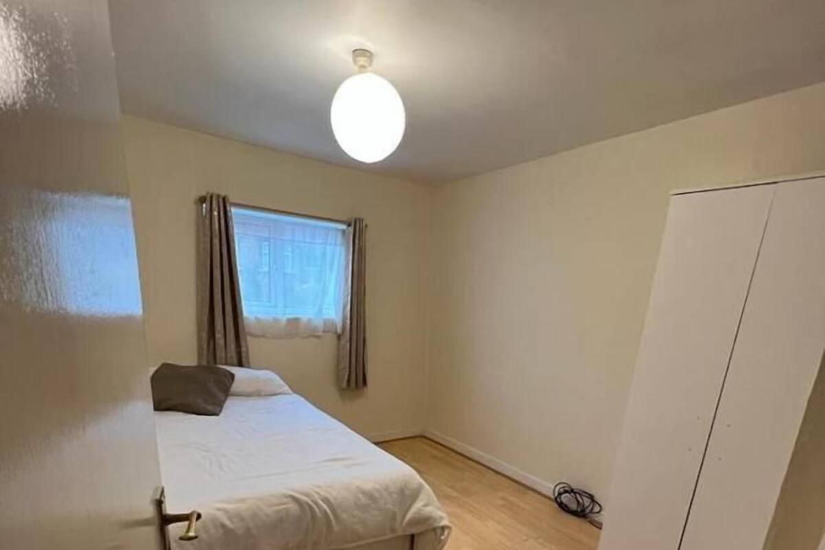 Un dormitorio con cama, armario, ventana con cortinas y luz en el techo.