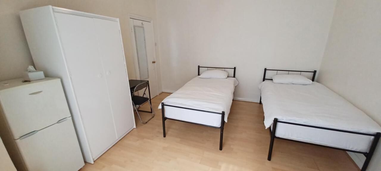 A small, sparsely furnished room with two single beds, a white wardrobe, and a small desk.