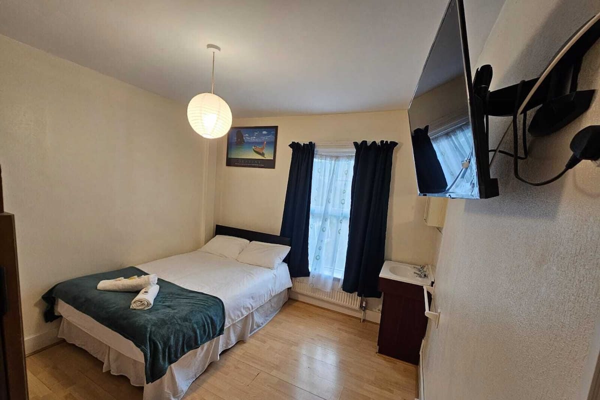 Un dormitorio pequeño y ordenado con una cama individual, una mesita de noche, un espejo y una ventana con cortinas.