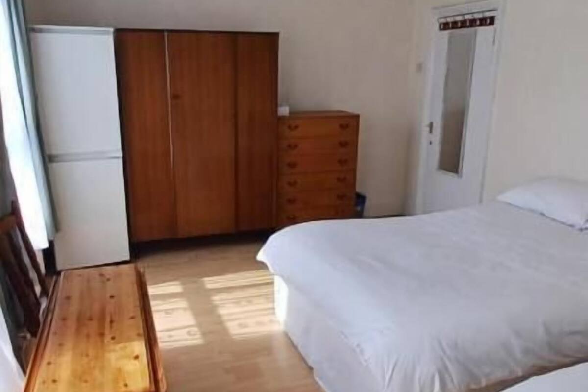 Una habitación con una mesa de madera, dos camas, un armario y una lámpara colgante.